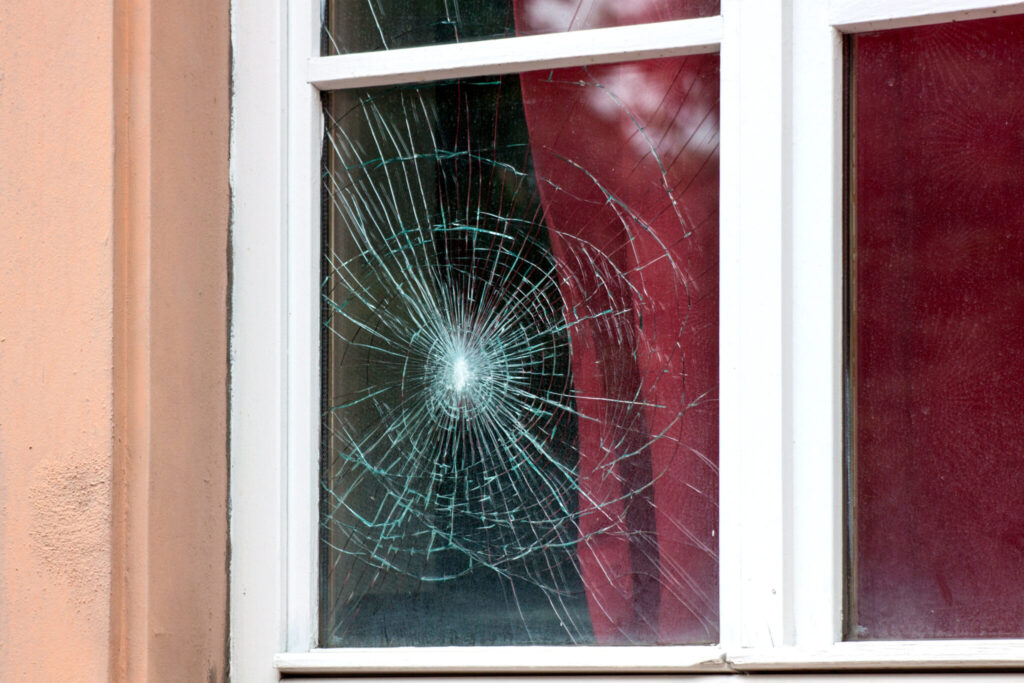 A window pane broken through, with cracks spreading from the hole