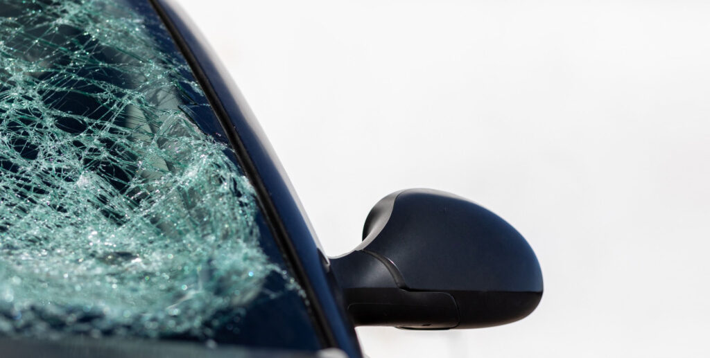 Heavily shattered windshield on a dark car, seen past the wing mirror